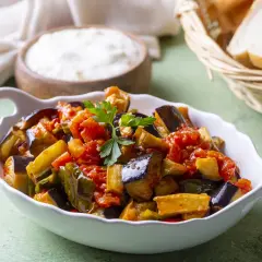 Melanzane al funghetto non fritte, un contorno saporito e leggero, servito in una ciotola bianca con pane e formaggio sullo sfondo.