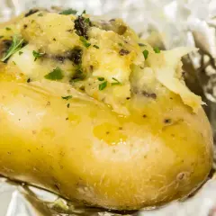 Patate ripiene al forno, dorate e fumanti, avvolte in carta stagnola, con un ripieno cremoso e erbe aromatiche.