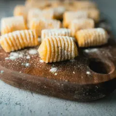 Gnocchi di patate ricetta originale pronti per essere cucinati, disposti su un tagliere di legno con un po' di farina sparsa.