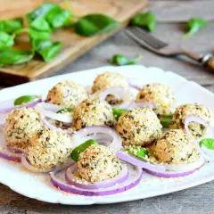 Deliziose polpette di ricotta impanate con semi di sesamo e erbe aromatiche, servite su un letto di cipolla rossa e foglie di basilico fresco.