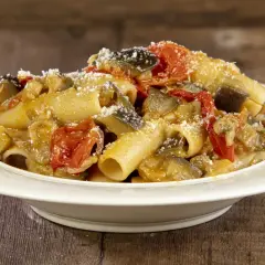 Piatto di pasta con melanzane e pomodorini, condita con formaggio grattugiato, su un tavolo di legno.