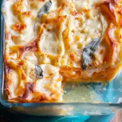 Lasagne con zucca dorate e filanti, guarnite con foglie di salvia, in una teglia di vetro.