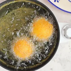 Arancini di riso dorati friggono nell'olio bollente, creando un profumo invitante.