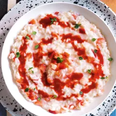 Un cremoso risotto alle fragole, guarnito con salsa di fragole e foglioline verdi.
