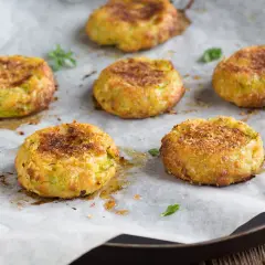 Sei polpette di zucchine dorate e croccanti, appena sfornate, su carta da forno.