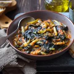 Cicoria in padella, un piatto rustico e saporito, servito in una ciotola con pane fresco e un bicchiere d'acqua.