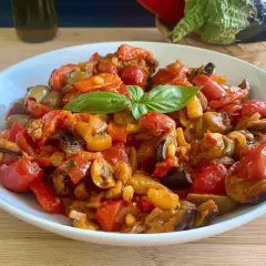 Caponata ricetta semplice: un piatto colorato con melanzane, peperoni, pomodorini e basilico fresco.