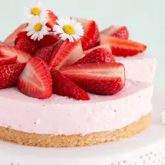Delizioso cheesecake alle fragole, decorato con fragole fresche e fiorellini bianchi.