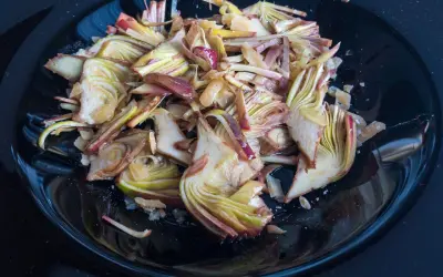 Un piatto nero lucido pieno di un'appetitosa insalata di carciofi crudi, tagliati finemente e conditi.