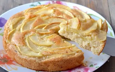 Una fetta di torta di mele senza uova, con mele a fette disposte a spirale sulla superficie dorata.