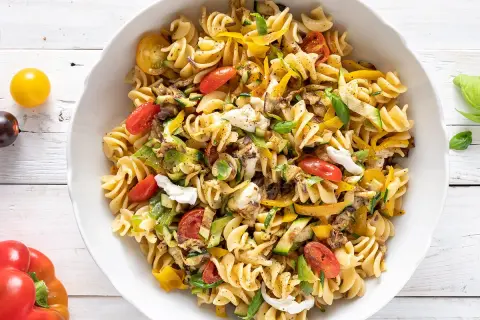 Insalata di pasta con fusilli, pomodorini, zucchine, peperoni gialli e mozzarella fresca. Un piatto colorato e gustoso.