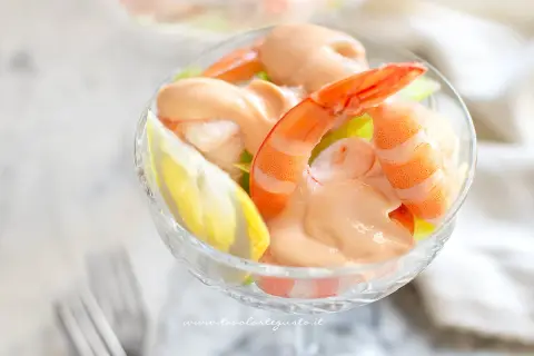 Un delizioso cocktail di gamberi servito in una coppa di vetro, con gamberi succulenti, salsa rosa e una fetta di limone.