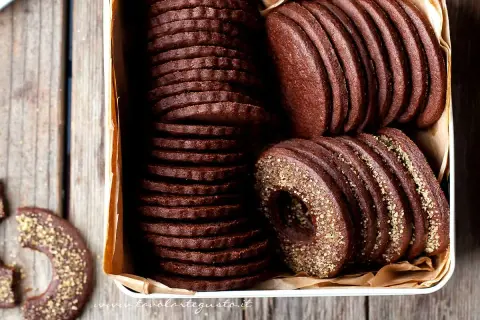 Una scatola piena di deliziosi biscotti al cacao, alcuni impilati in modo ordinato, altri con un bordo dorato croccante.
