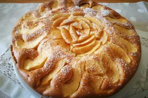 Deliziosa torta di mele senza glutine, con mele disposte a rosa al centro e spolverata di zucchero a velo.