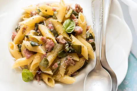 Penne con zucchine e salsiccia, un piatto gustoso e facile da preparare, guarnito con basilico fresco e parmigiano.