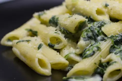 Penne cremose con spinaci freschi e parmigiano grattugiato, un piatto semplice e gustoso.