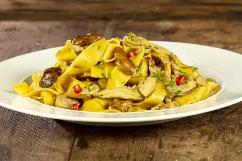 Un piatto invitante di tagliatelle ai funghi porcini, guarnite con peperoncino e prezzemolo fresco, su un tavolo di legno rustico.