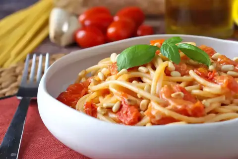 Un piatto invitante di spaghetti con pomodorini freschi, pinoli tostati e basilico, pronto per essere gustato.