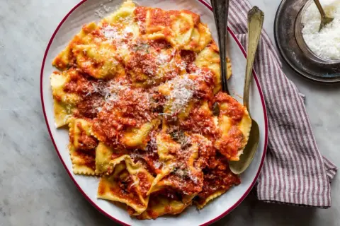 Piatto di tortelli di patate fatti in casa, conditi con sugo rosso e parmigiano grattugiato, pronti per essere gustati.