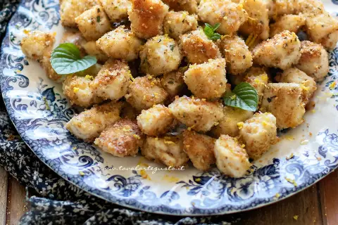 Bocconcini di pollo al forno dorati e croccanti, guarniti con scorza di limone e foglie di menta fresca su un piatto decorato.