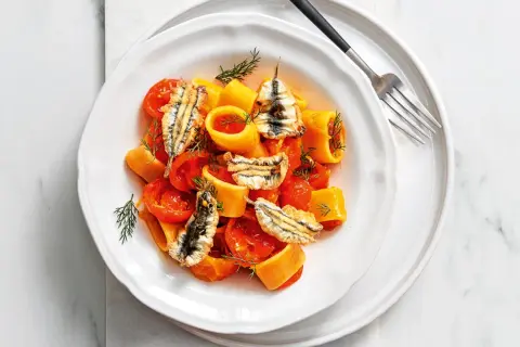 Piatto di pasta con pomodorini e croccanti alici fresche, guarnito con aneto.