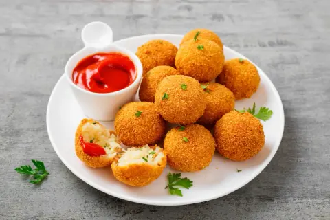 Deliziose polpette di riso dorate e croccanti, servite con salsa di pomodoro e prezzemolo fresco.