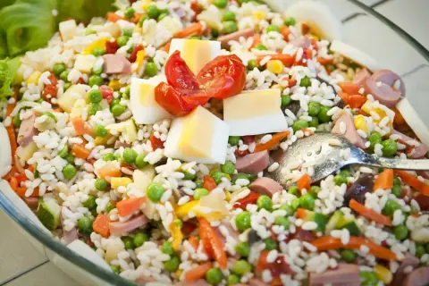 Insalata di riso ricca di ingredienti: piselli, carote, uova sode, pomodorini e salumi. Perfetta per un pasto fresco e completo.