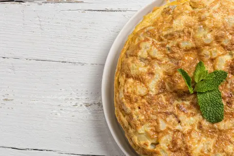 Frittata di cipolle dorata e soffice, guarnita con menta fresca, su un tavolo di legno bianco.
