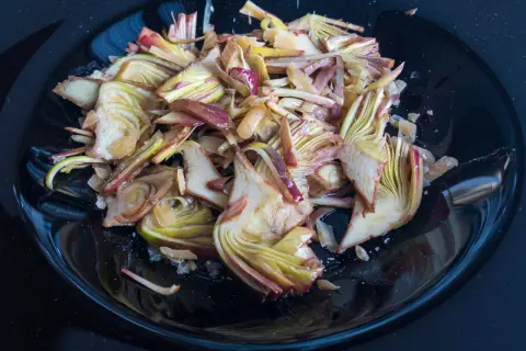 Un piatto nero lucido pieno di un'appetitosa insalata di carciofi crudi, tagliati finemente e conditi.