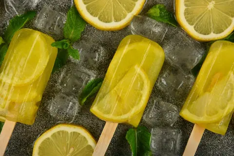 Ghiaccioli al limone con fette di limone e foglie di menta, circondati da cubetti di ghiaccio. Rinfrescante e gustoso.