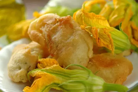 Fiori di zucca in pastella dorati e croccanti, guarniti con i loro stessi fiori freschi.