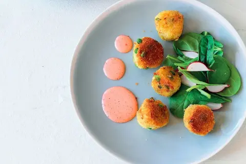 Deliziose polpette di verdure dorate, servite con insalata fresca e salsa rosa su un piatto azzurro.