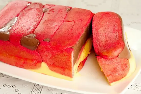 Una fetta di zuppa inglese tradizionale, con savoiardi rossi, crema al cioccolato e crema gialla.