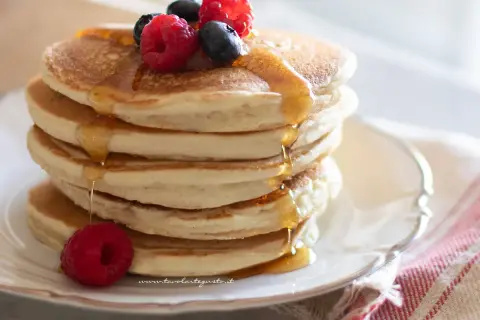 Pancakes senza uova soffici e dorati, inzuppati di sciroppo d'acero e guarniti con frutti di bosco freschi.