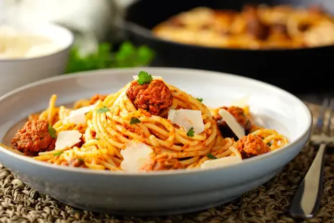 Un piatto invitante di spaghetti con ragù di salsiccia, guarnito con scaglie di parmigiano e prezzemolo fresco.