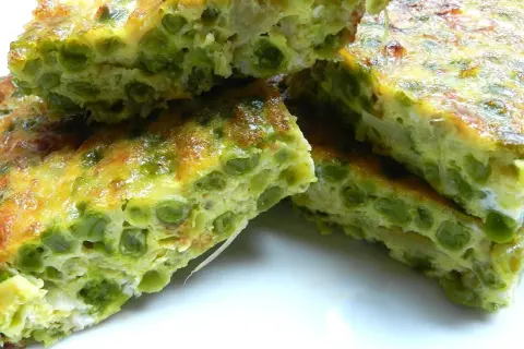 Fette di frittata di piselli, dorata e soffice, con piselli verdi ben visibili nell'uovo.