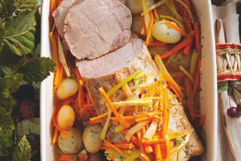 Succulento maiale in agrodolce con carote julienne, cipolline e erbe aromatiche in una teglia bianca.