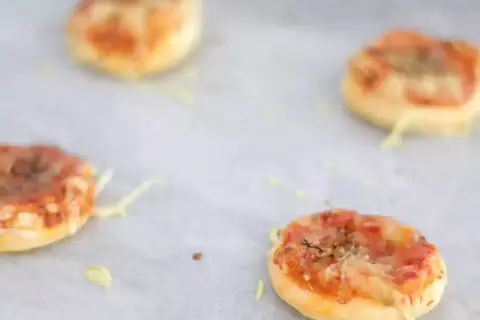 Quattro pizzette di pasta sfoglia appena sfornate, dorate e filanti, pronte per essere gustate.