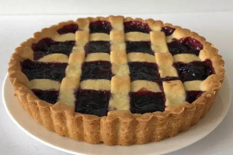 Una crostata di marmellata con una griglia di pasta dorata e un ripieno scuro e invitante.