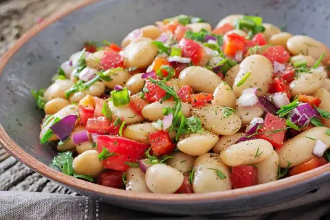 Insalata di fagioli bianchi, pomodori, cipolla rossa e erbe fresche in una ciotola rustica. Un piatto leggero e saporito.