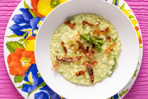 Un cremoso risotto asparagi e speck, guarnito con punte di asparagi freschi e croccanti sfoglie di speck.