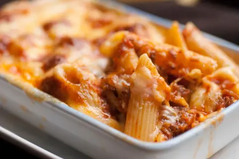 Un invitante piatto di pasta al forno, con penne ricoperte da un ricco sugo e formaggio filante, pronto per essere gustato.