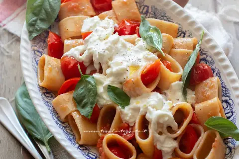 Piatto di pasta con pomodorini e burrata cremosa, guarnito con basilico fresco. Un'esplosione di sapori mediterranei.