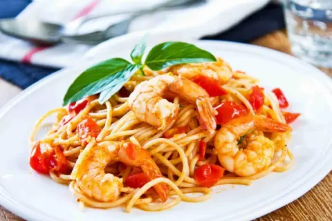 Un piatto invitante di spaghetti con gamberi succulenti e pomodorini freschi, guarnito con basilico.