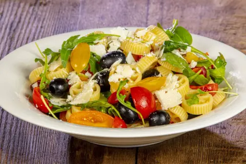 Pasta alla crudaiola con pomodorini, olive nere, rucola e scaglie di parmigiano. Fresca e colorata, un piatto estivo perfetto.