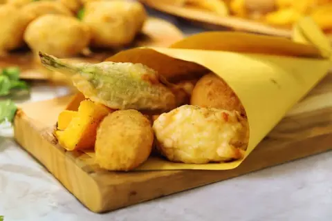 Un cono di carta gialla contiene fritti misti, tra cui spicca una mozzarella in carrozza filante, accompagnata da verdure pastellate e polenta fritta.