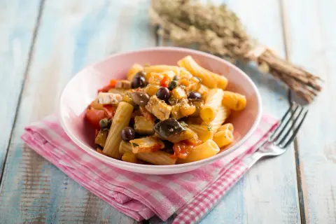 Piatto di pasta con melanzane, tonno, pomodorini e olive nere, condito con erbe aromatiche.