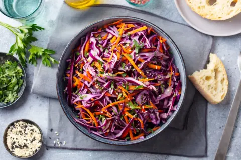 Una fresca insalata di cavolo rosso e carote, guarnita con erbe aromatiche e semi di sesamo, pronta per essere gustata.