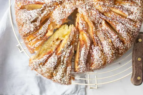 Deliziosa torta di mele in friggitrice ad aria, cosparsa di zucchero a velo, con una fetta tagliata che rivela il morbido interno.