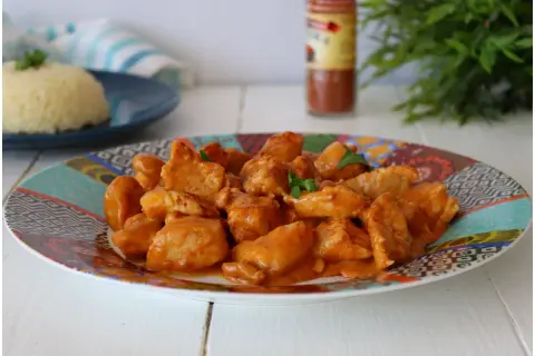Succulento pollo alla paprika in una salsa cremosa, servito su un piatto colorato con riso bianco sullo sfondo.